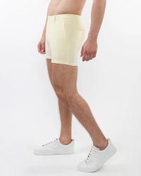 Person wearing light yellow shorts and white sneakers on a white background